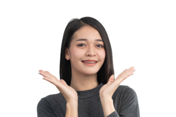 Smiling young woman showing excitement with hands raised in a cheerful gesture wearing a gray sweater and sporting braces on her teeth against a plain background