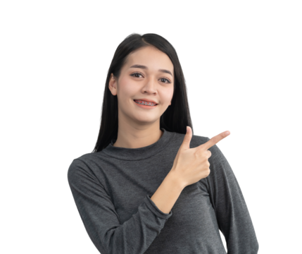 Young woman in gray long-sleeve shirt smiling and pointing with finger, casual pose against white background, promoting cheerful and friendly atmosphere