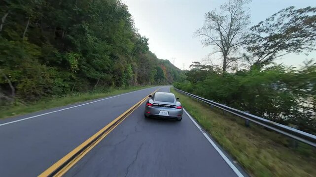 Aerial close following behind grey Sports Car nearby a river at sunset, US National Park
