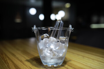 Ice Bucket with Tongs on Wooden Table in Dimly Lit Modern Restaurant Interior