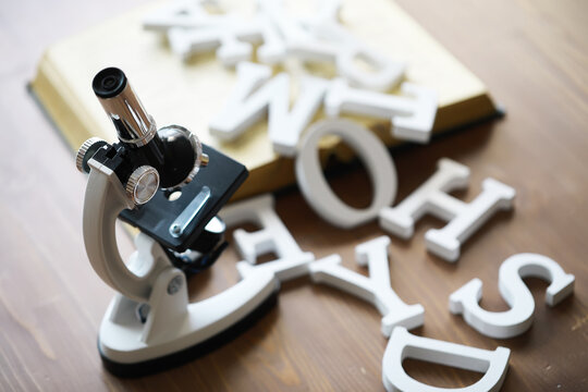 Microscope with Scattered Wooden Letters and Book on Wooden Table - Education and Science Concept