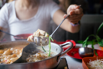 Close-up of a hand using a ladle to serve ingredients from a steaming hot pot