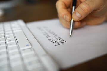 Hand Signing Last Will and Testament Document on a Desk Next to a White Keyboard