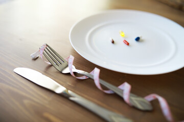 Diet Concept: Empty Plate with Pills and Measuring Tape Around Cutlery on Wooden Table