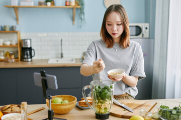 Teenage girl preparing a recipe in the kitchen while recording a cooking blog with a smartphone