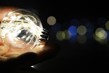 Hand Holding Illuminated Glass Bulb with Colorful Bokeh Background - Creative Lighting Concept