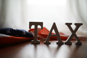TAX Letters on Wooden Surface with American Flag Background - Financial Concept