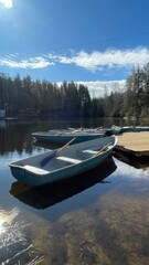 Obraz premium Boats with Oars on Dock at Wooden Pier – Sunny Morning on Calm Lake with Pine Trees & Peaceful Atmosphere