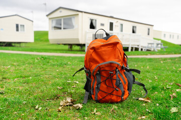 Bright orange backpack rests on green grass with modern mobile homes in the background during an...