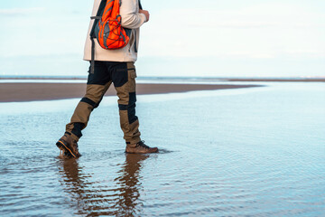 Person walks along a shallow beach at low tide with a backpack during a clear, sunny day, enjoying...
