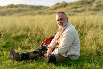Older man sitting on grass in a field during late afternoon, surrounded by tall grass and gentle...