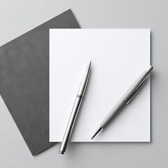 Flatlay of blank white stationery, two silver pens, and a dark gray envelope on a light gray background