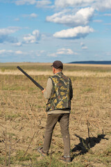 Mature man hunter with gun while walking on field.