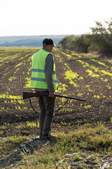 Mature man hunter with gun while walking on field.