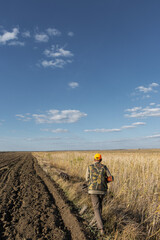 Mature man hunter with gun while walking on field.
