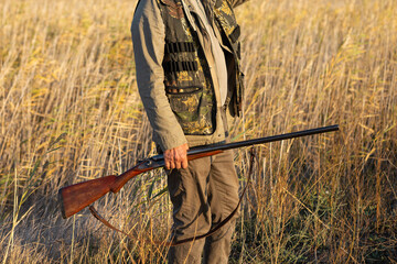 Mature man hunter with gun while walking on field.