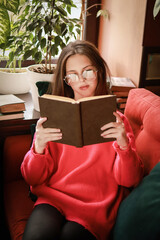 The girl is reading a book while sitting on the sofa.