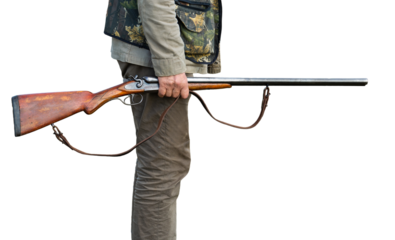 Mature man hunter with gun while walking on field.