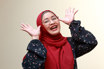 An Asian Muslim lady raising both of her hands to her face and laughing. Happy and playful expression.