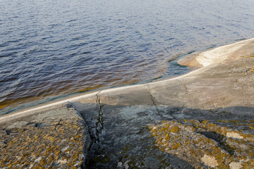 A gently sloping rock surface with moss and visible cracks leads into clear lake water, under soft evening sunlight.