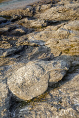 Close-up of layered rock formations on a lakeside, lit by warm evening light with visible cracks,...