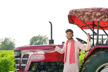 young indian farmer standing with tractor at field