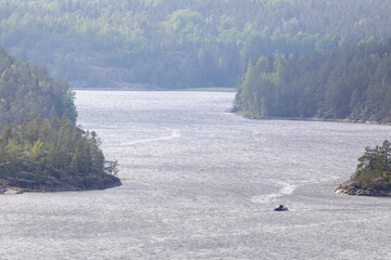 Small inflatable boat travels through a wide river or lake passage surrounded by dense green forest...