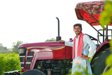 young indian farmer standing with tractor at field
