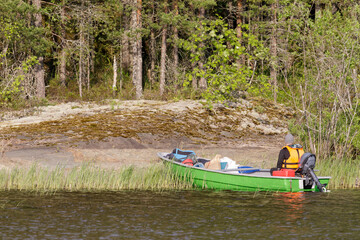 Person in an orange life vest arrives at a forested shoreline in a green motorboat filled with...