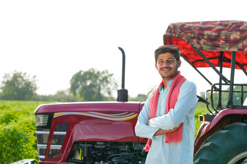 young indian farmer standing with tractor at field