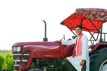 young indian farmer standing with tractor at field