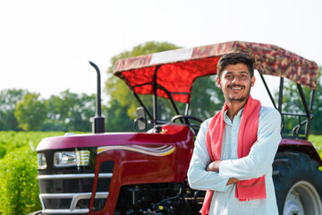 young indian farmer standing with tractor at field