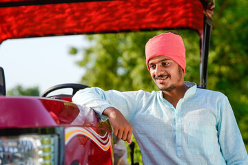 young indian farmer standing with tractor at field