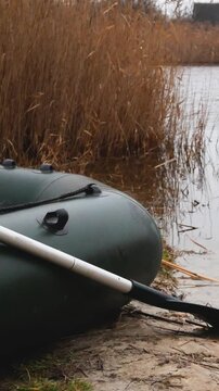 An inflatable boat with lowered oars stands on the sandy shore of the lake near the water in late autumn. Walks in the wild in late autumn