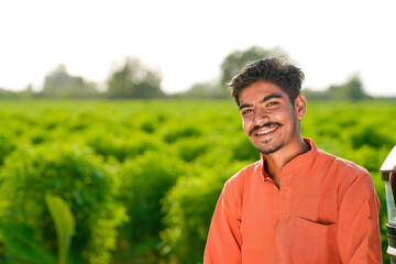 young indian farmer standing at green agricultural field
