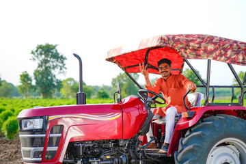 young indian farmer sitting with tractor at field