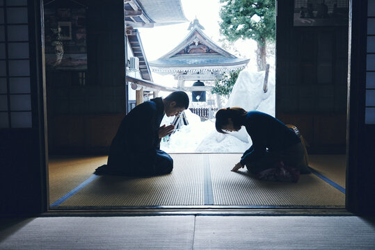 雪の日本寺院で互いに礼を交わす僧侶と女性