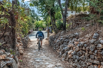 A cyclist rides along a rustic stone path amid trees and ancient walls at Alanya Castle. The peaceful setting highlights the site's scenic, historic charm. Alanya, Turkey - October 24, 2020