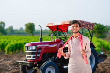 young indian farmer standing with tractor at field