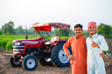 two young indian farmer standing together with tractor at field