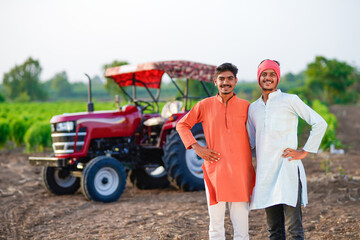 two young indian farmer standing together with tractor at field