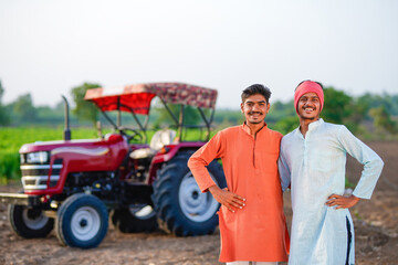 two young indian farmer standing together with tractor at field