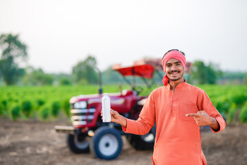 Young indian farmer showing liquid fertilizer bottle at field