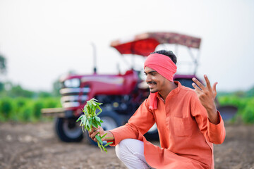 young indian farmer holding plant sitting at field