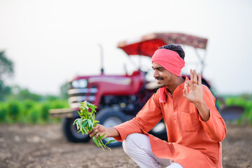 young indian farmer holding plant sitting at field