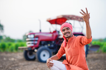 young indian farmer sitting with tractor at field