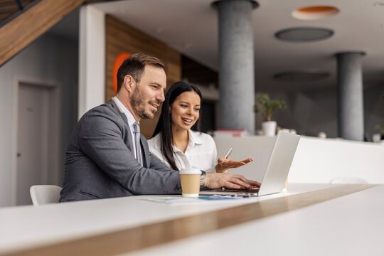 Two professional businesspeople sitting at corporate office and doing statistics on laptop.