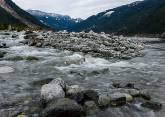 Mountain river flows over smooth stones in a serene valley surrounded by peaks