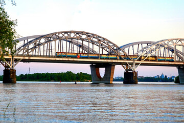 Obraz premium A large railway bridge with passenger train on an evening calm river