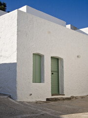 Traditional Greek house with white facade and olive green closed shutters and door, captured in soft natural light.